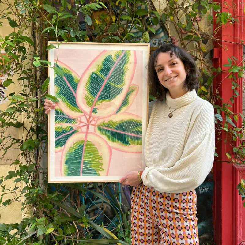 Magali Reynard tenant un tirage d'art grand format 50x70cm représentant un ficus elastica au pastel, tons vert et rose